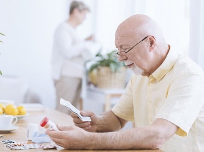 Ein &auml;lterer Mann liest eine Packungsbeilage f&uuml;r ein cholesterinsenkendes Medikament.