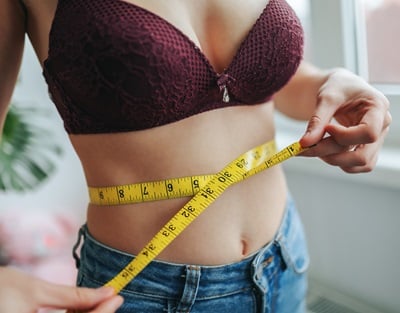 Eine Frau misst ihre Taille mit einem Ma&szlig;band.