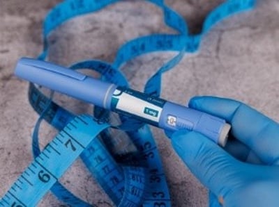 En h&aring;nd med bl&aring; handsker pr&aelig;senterer en Ozempic-pen og et m&aring;leb&aring;nd