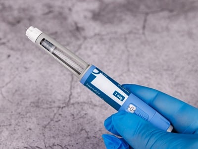 Hand mit blauen Handschuhen h&auml;lt Semaglutid-Pen