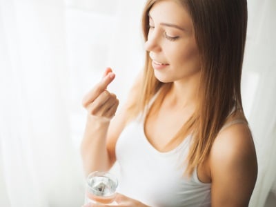 Eine junge Frau nimmt eine Antibabypille l&auml;chelnd ein